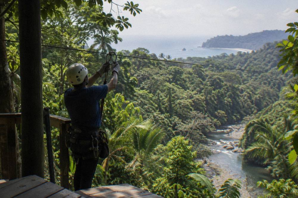 Guide clipping a carabiner to a zipline cable at a wooden platform above the forest canopy