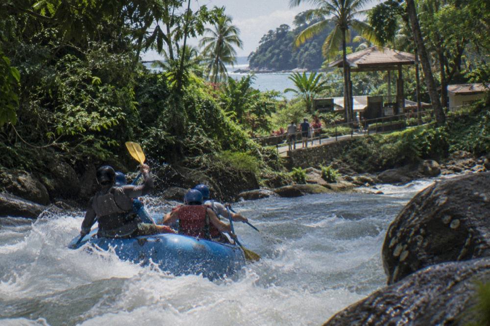 A raft cutting through a foamy rapid between walls of tropical forest