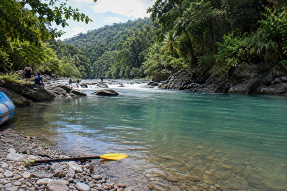 A calm turquoise pool between rapids, forested hills rising on both banks