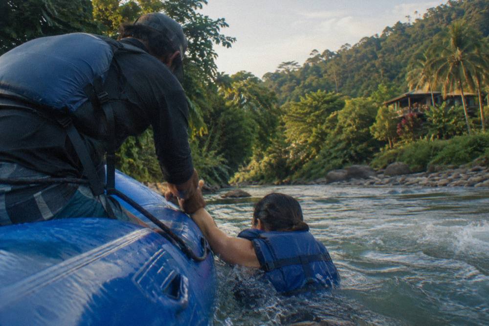 Raft guide pulling a swimmer in a life jacket back over the raft tube
