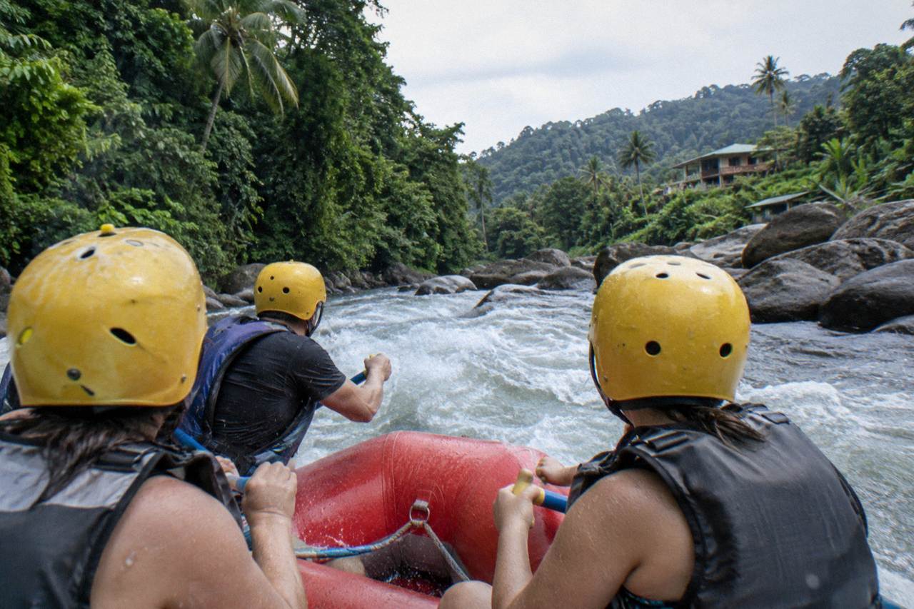 Inflatable raft crossing a green rainforest rapid with paddlers holding on