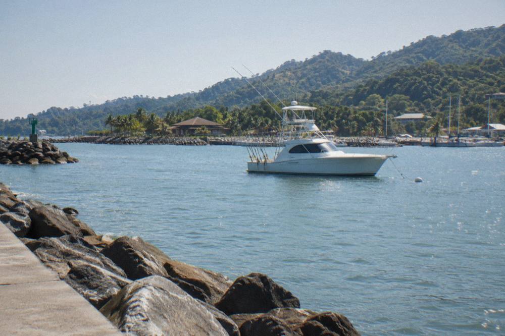 Charter fishing boat anchored near rocky coastline with rods secured along the rail