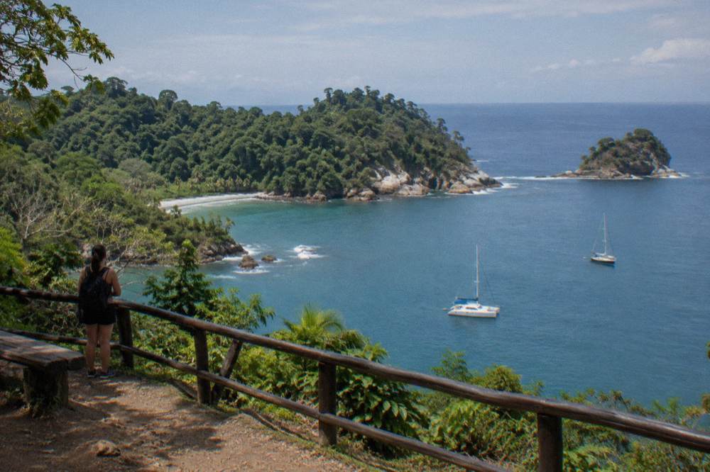 Catamaran and sailboat anchored in clear blue bay near forested headland