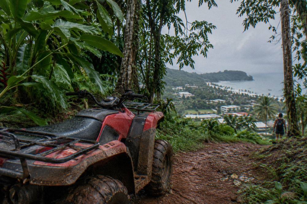 Four-wheeler parked on a muddy red-dirt trail between tall rainforest trees