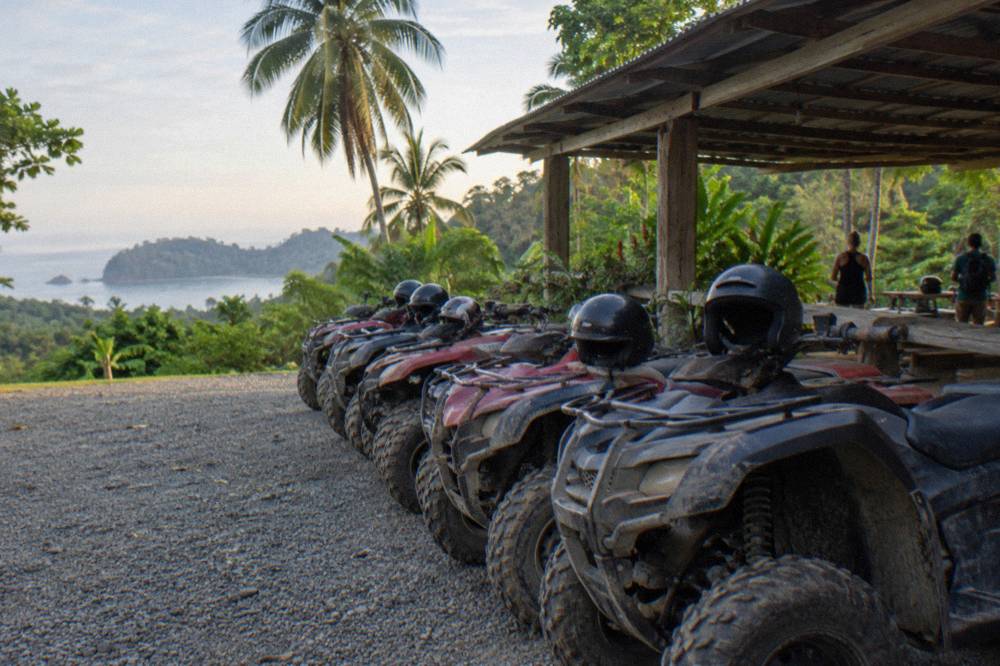Row of parked four-wheelers lined up on gravel beside a wooden briefing shelter