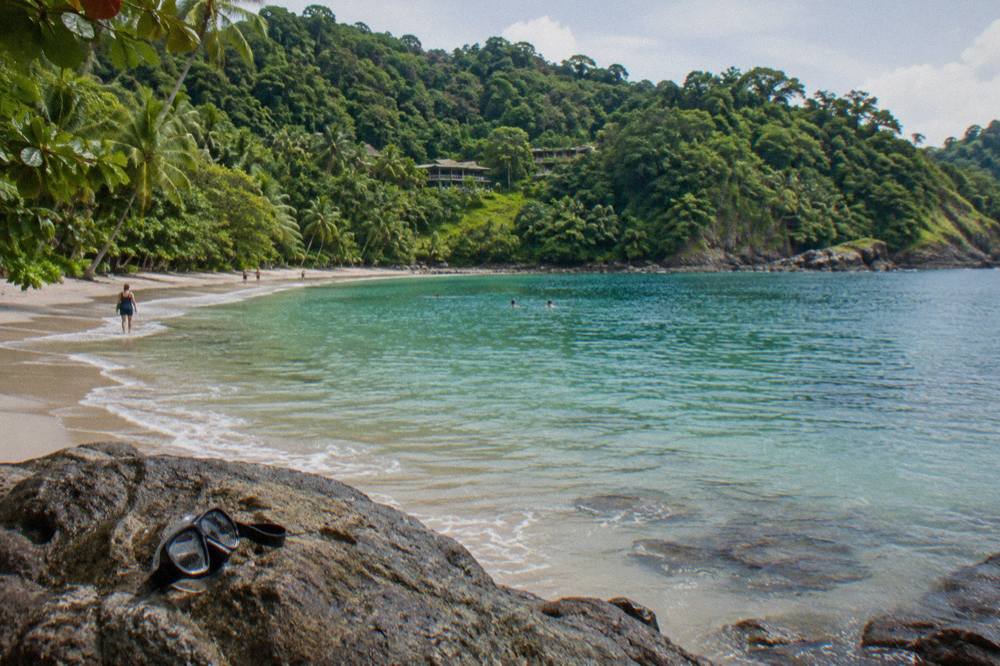 Calm turquoise cove with rainforest covered hills rising directly behind a strip of pale sand