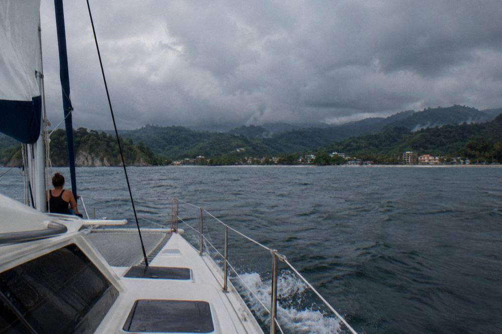 A catamaran under way on open water with rain clouds over distant hills