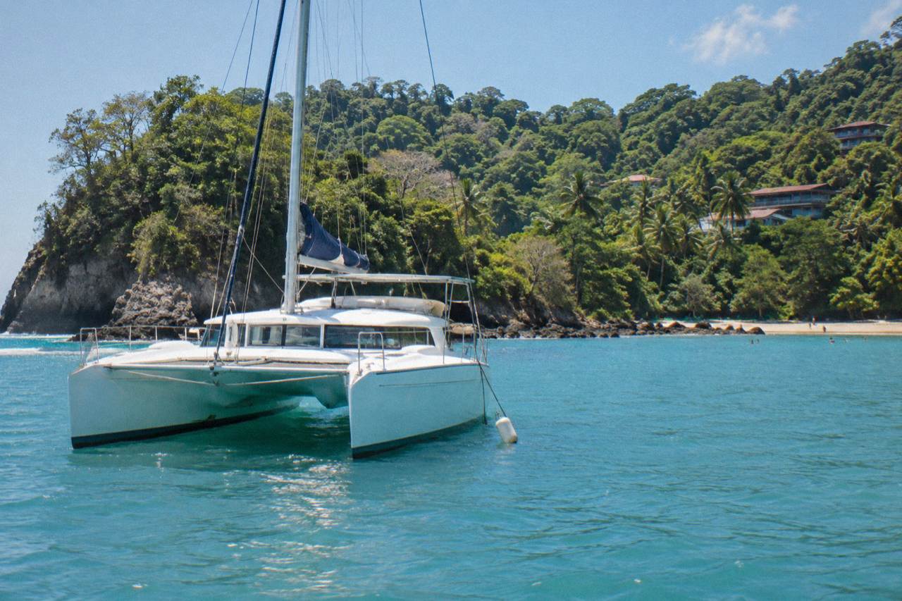 A catamaran anchored in a calm Pacific bay near Manuel Antonio with green forested hills behind it