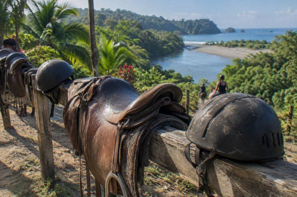 Riding helmets and saddles arranged on a ranch fence rail