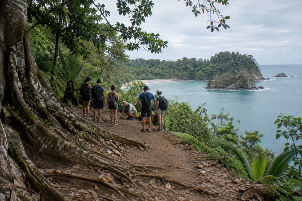 A small group of visitors gathered on a shaded park trail listening to a guide