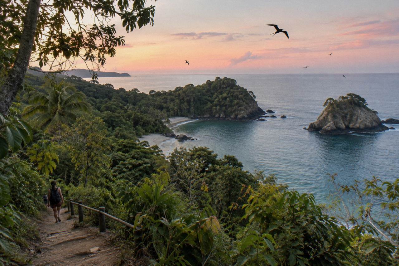 Rainforest canopy and a winding dirt trail above a Pacific bay at Manuel Antonio National Park