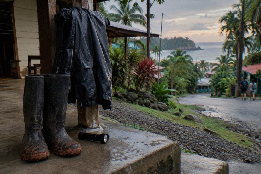 Rubber boots and a rain jacket drying beside a flashlight on a lodge step
