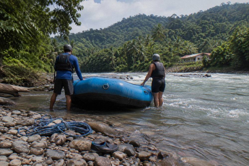 Inflatable raft held by guides at a river put-in below rainforest hills