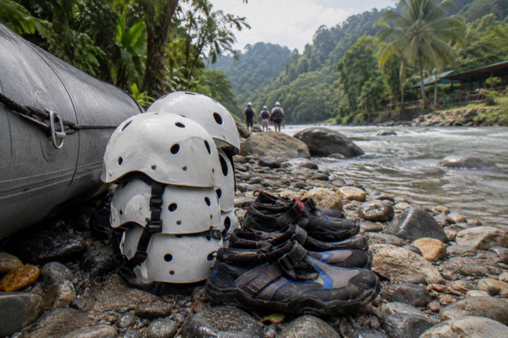 Dry bag and helmets arranged on riverbank stones beside a raft