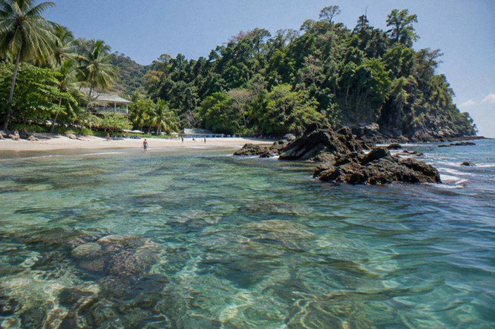 Rocky headland meeting clear shallow water with reef visible below the surface