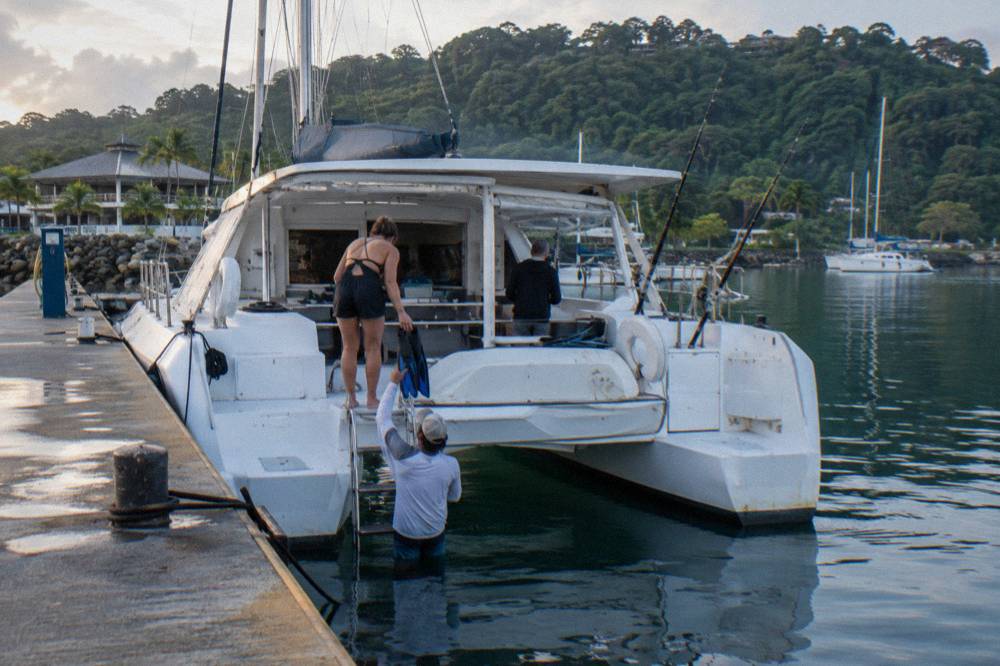 Catamaran moored in a quiet bay with snorkelers entering the water from the stern