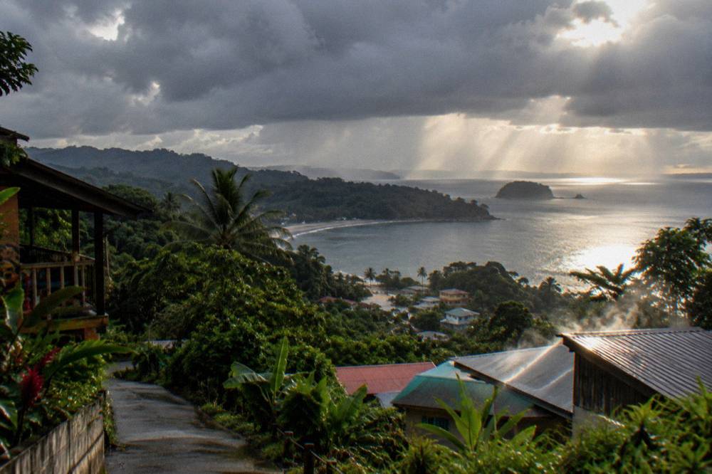 Rain clouds breaking over dark green coastal hills above a calm bay