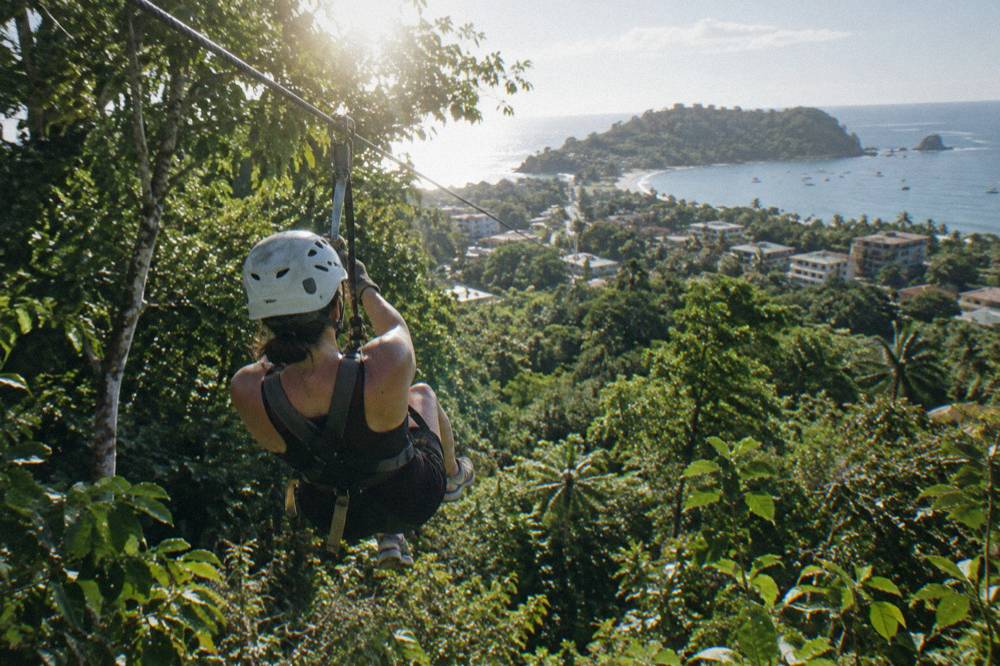 Person in helmet and harness riding a zipline above dense green rainforest