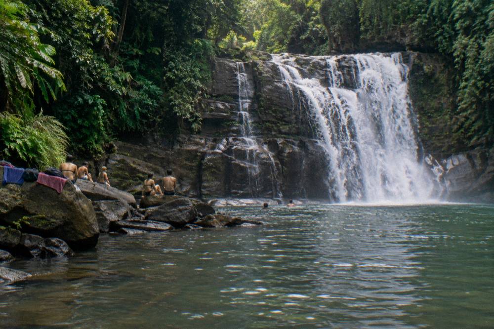 Visitors resting on rocks beside a wide cascade in jungle surroundings