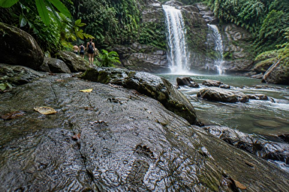 Dry bag and water shoes resting on a rock beside a jungle stream
