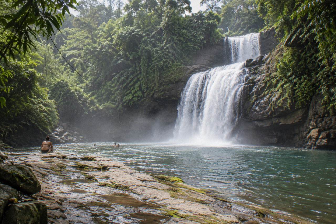 Wide waterfall dropping into a large forest pool with a rocky ledge in the foreground