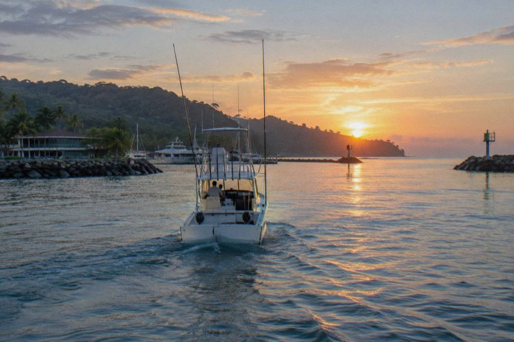 A sport fishing boat heading out over calm blue Pacific water at sunrise
