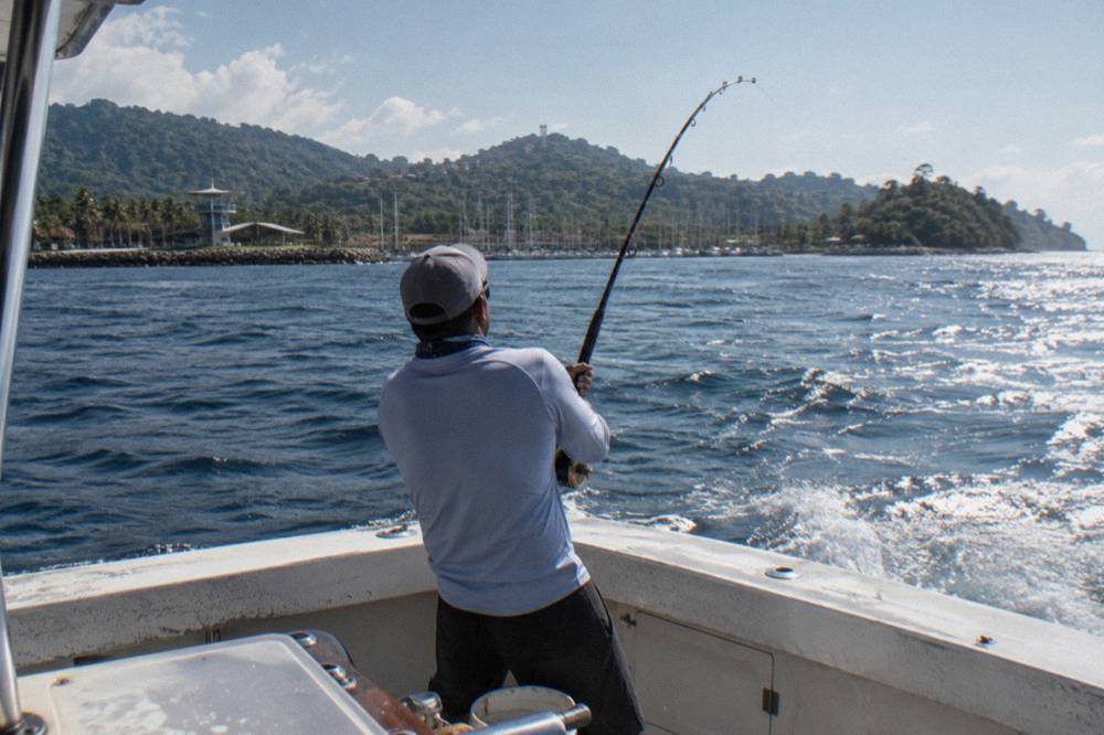 An angler standing at the stern of a fishing boat holding a rod over open ocean