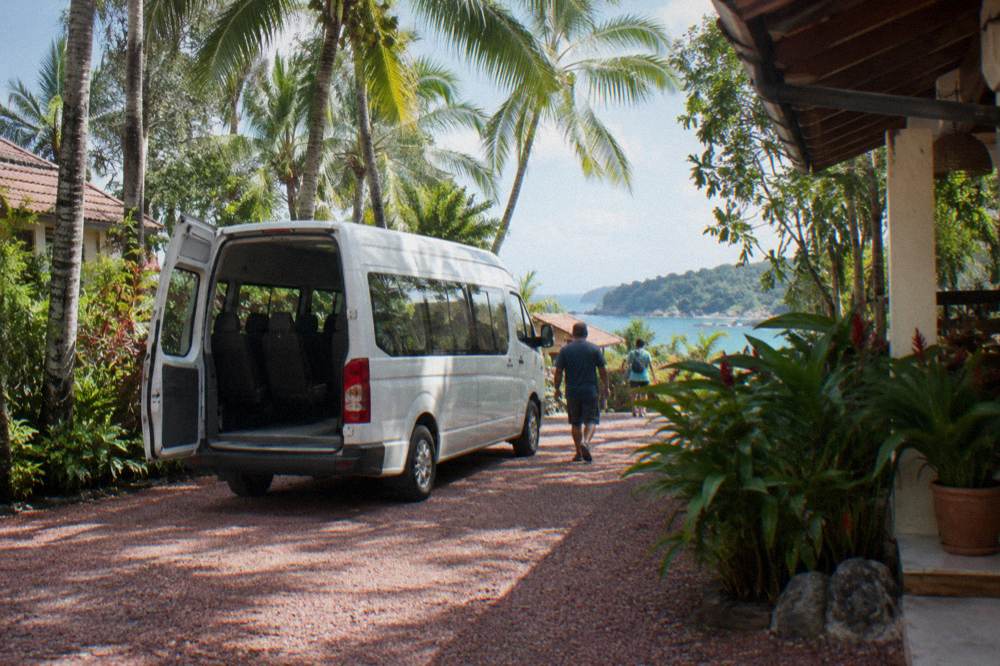 Minibus shuttle parked beside palm trees at a hotel driveway entrance