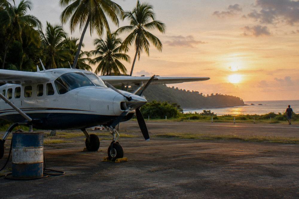 Small propeller aircraft on a regional airstrip beside palm trees near the coast
