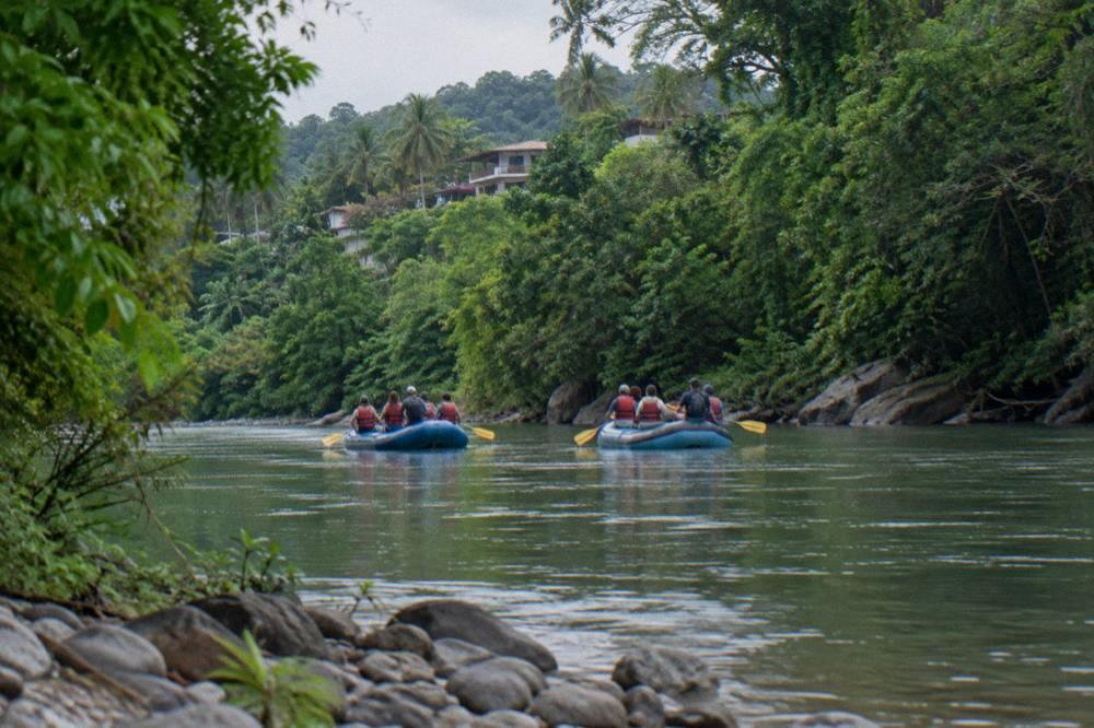 Two rafts floating side by side on calm green water between forested banks