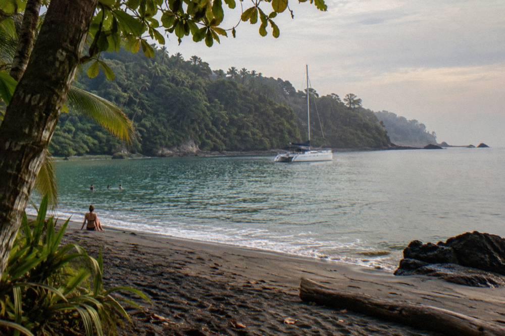 A catamaran anchored in a calm bay with forested hills along the shoreline