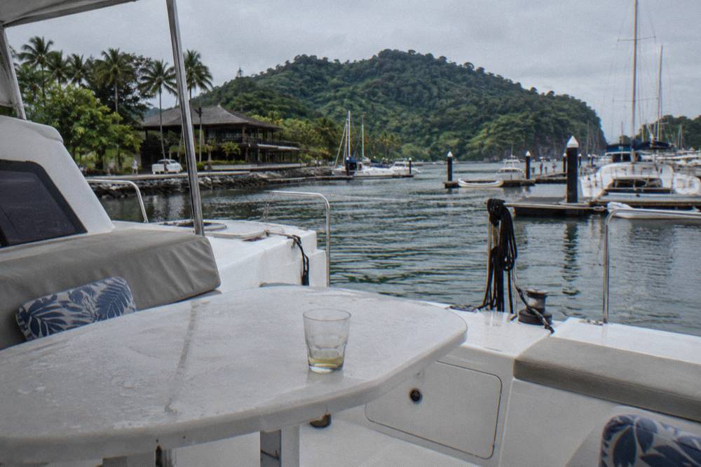 Open deck of a catamaran moored at a marina with forested hills behind