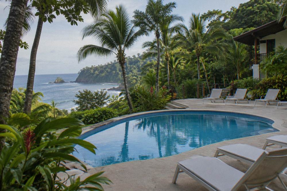 A beachfront hotel pool with white loungers among palms and rainforest on the Manuel Antonio coast